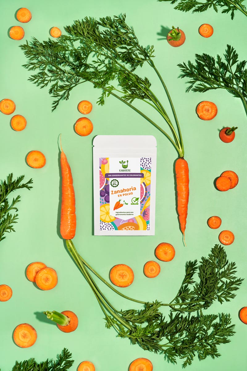 Captivating flat lay photograph featuring a white packaging filled with a finely powdered blend of fresh seasonal ingredients. Surrounding the packaging, you'll find fresh carrots. This exquisite studio product photography showcases the essence of the Kamarere food brand.