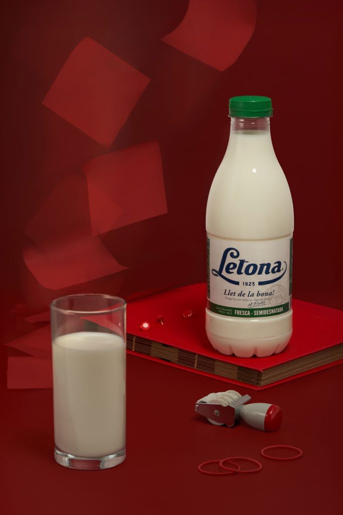 Milk bottle with glass of milk on red background and vintage surroundings. It features objects symbolizing childhood memories and shifting moments, capturing fragile balance and tension in a quiet, suspended scene rooted in personal narratives and fragmented past. By Irina Lokteva Pikalova (Irina Lopik).